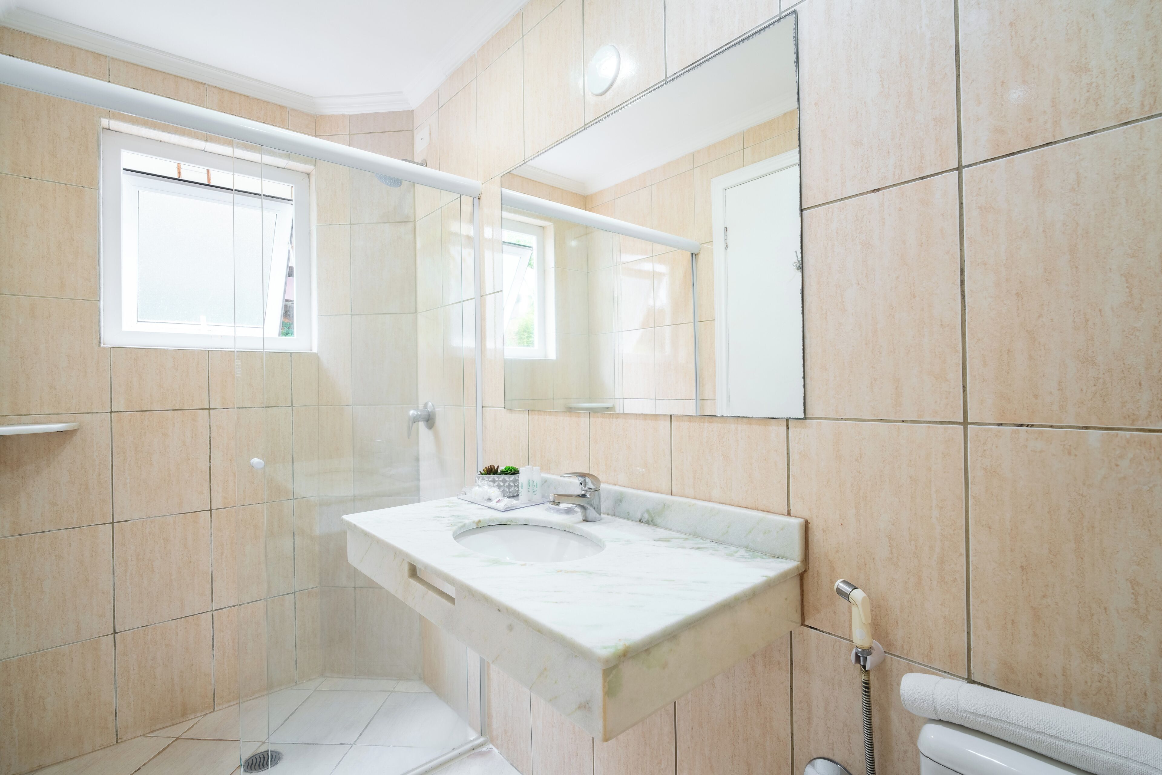 Un baño con ducha envuelta en vidrio, un lavabo con encimera de mármol y un espejo grande sobre el lavabo.