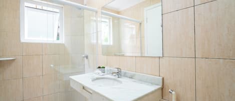 Un baño con ducha envuelta en vidrio, un lavabo con encimera de mármol y un espejo grande sobre el lavabo.