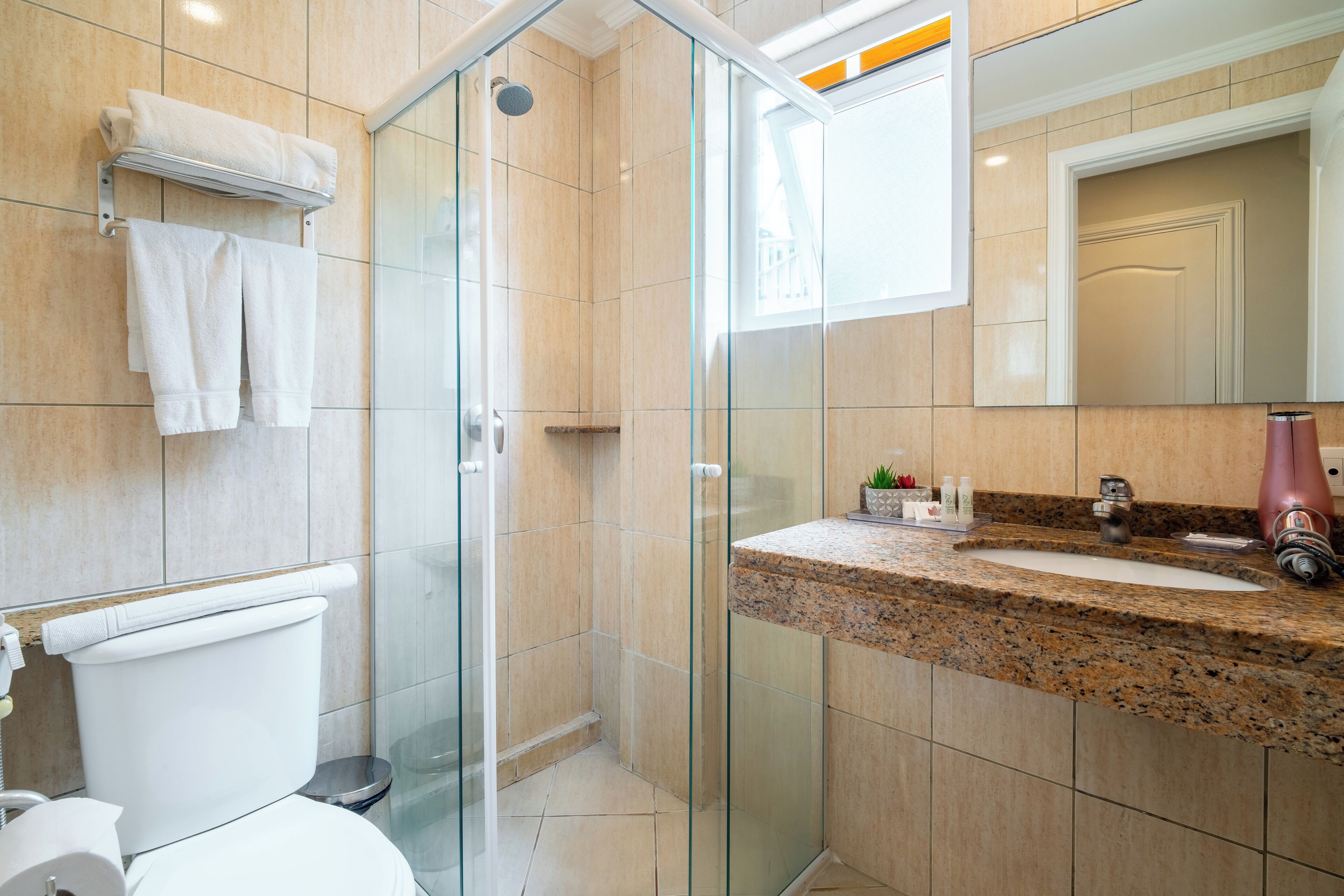 A modern bathroom with a glass-enclosed shower, a granite countertop sink, and a white toilet.