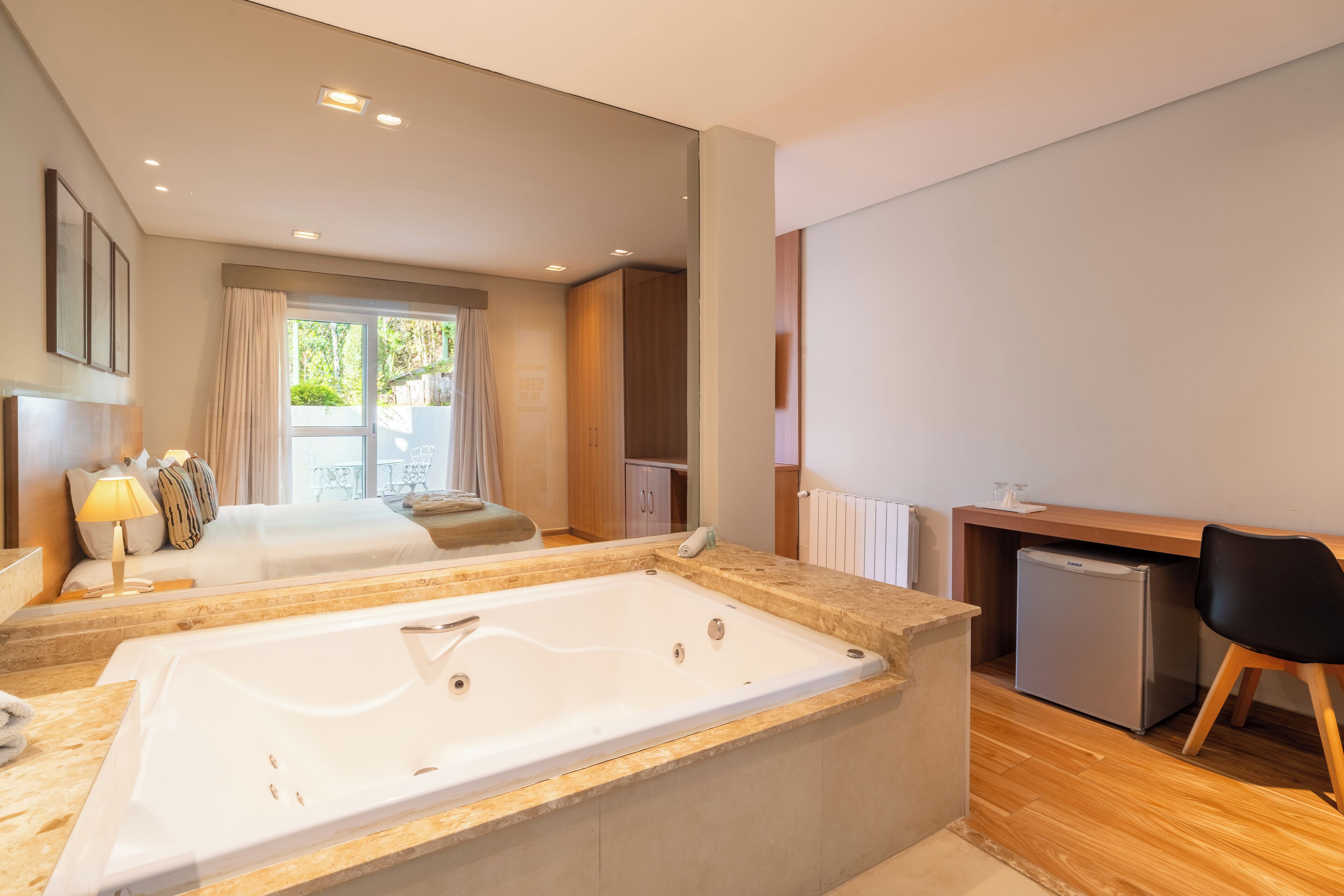 A modern hotel room with a large bathtub, a desk, and a chair.