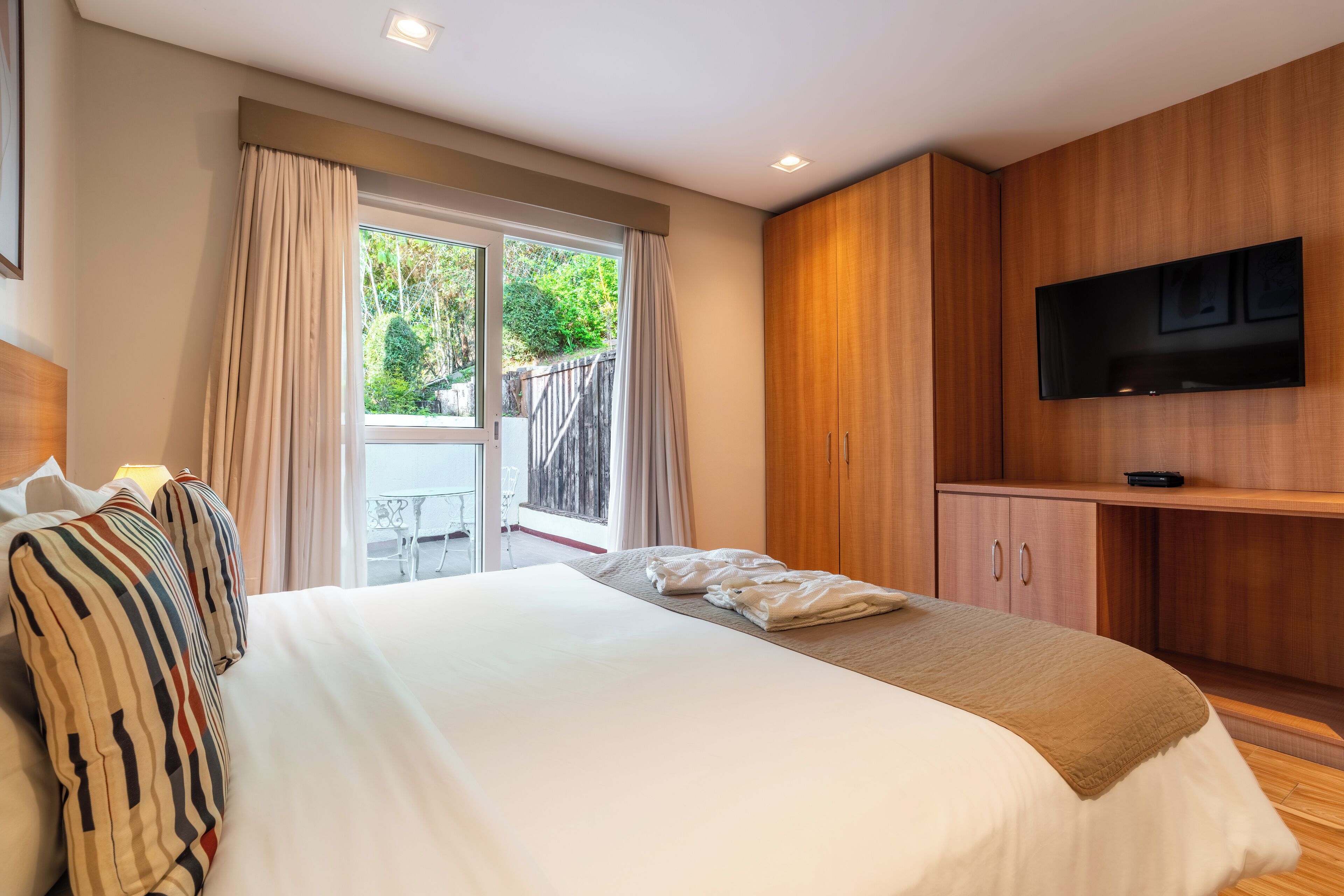Ein modernes Hotelzimmer mit einem großen Bett, einem Holzschrank und einem an der Wand befestigten Fernseher.