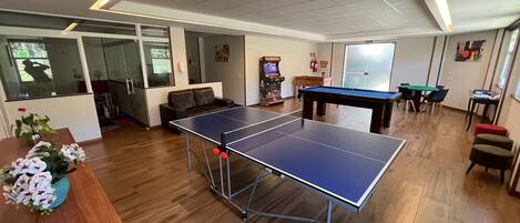 A room with a ping pong table, a sofa, a coffee table with flowers, and a pool table.
