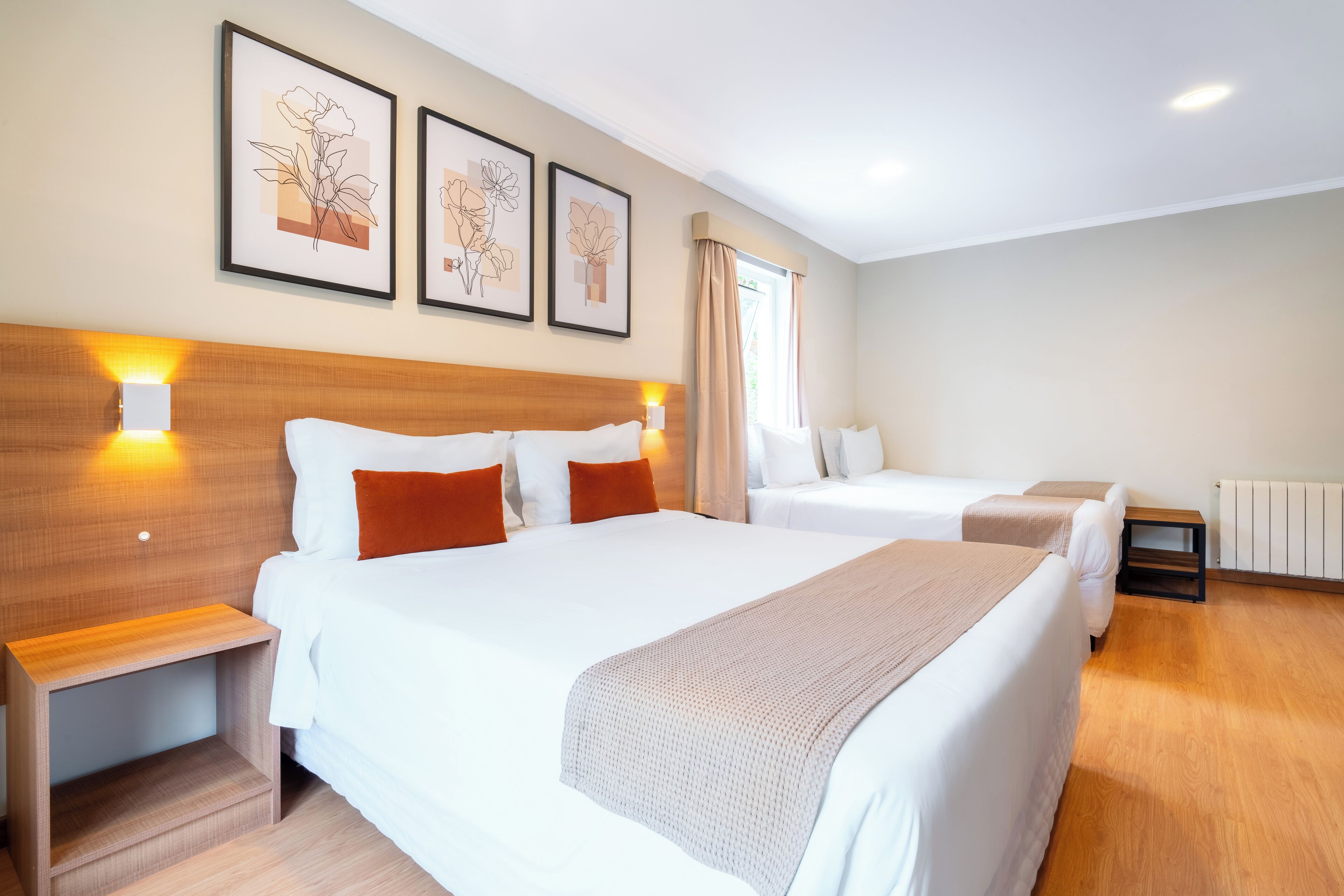Ein Hotelzimmer mit zwei Betten, einem Holzkopfteil, Nachttischen und an der Wand befestigter Kunst.