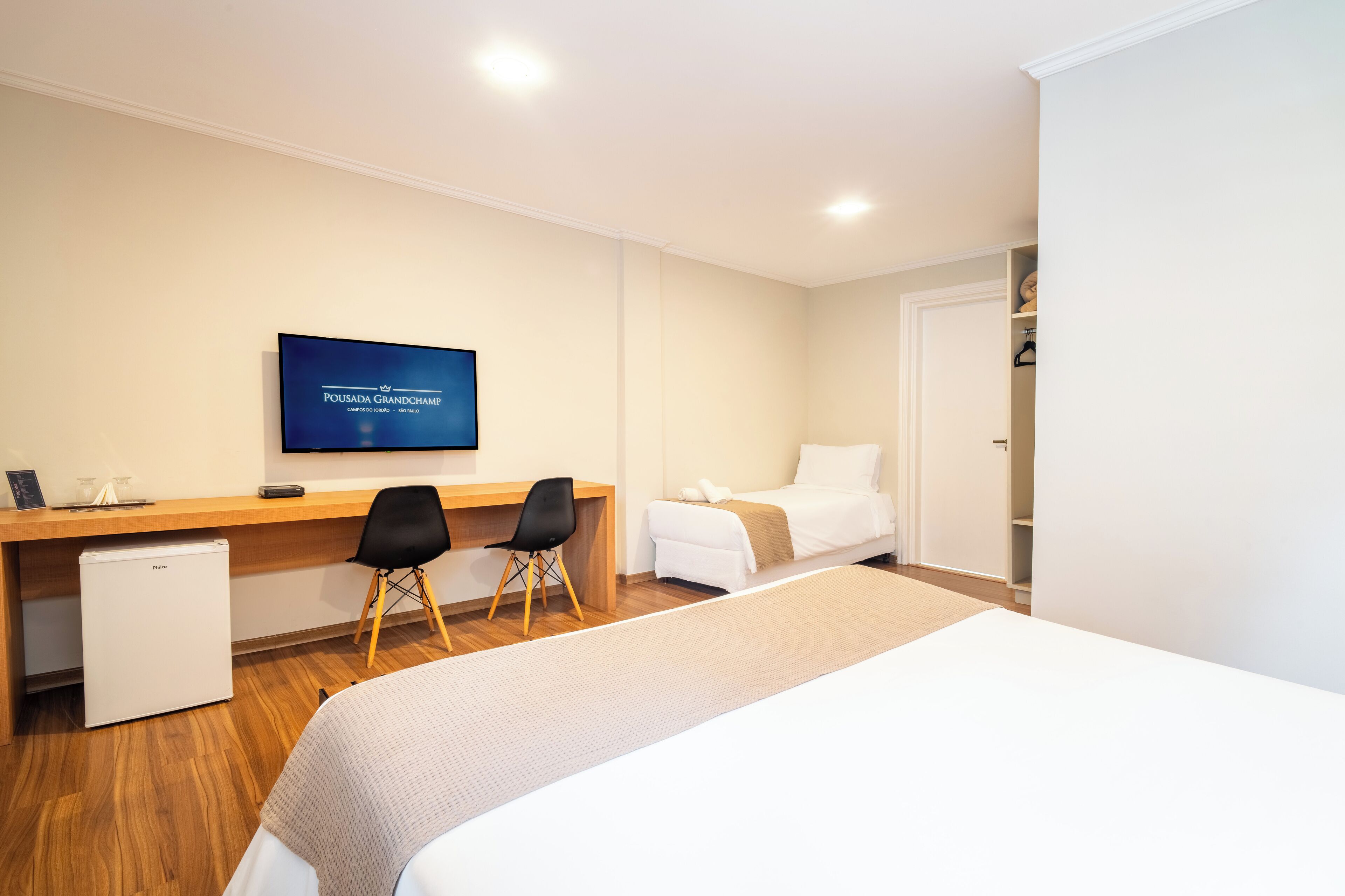 A hotel room with a bed, a desk, a chair, a television, and a small refrigerator.
