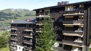 A multi-story residential building with balconies, a view of the surrounding landscape, and a mountain in the background.