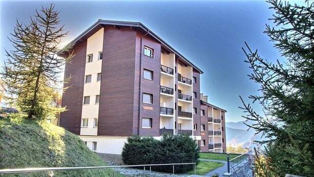 A multi-story hotel with a modern design, featuring balconies and a view of the surrounding landscape.