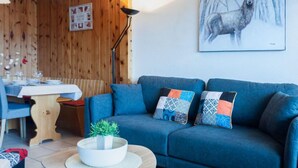 A cozy living room with a blue sofa, a wooden dining table, and a painting of a deer. - Christiania I I4 by Interhome (Nendaz)