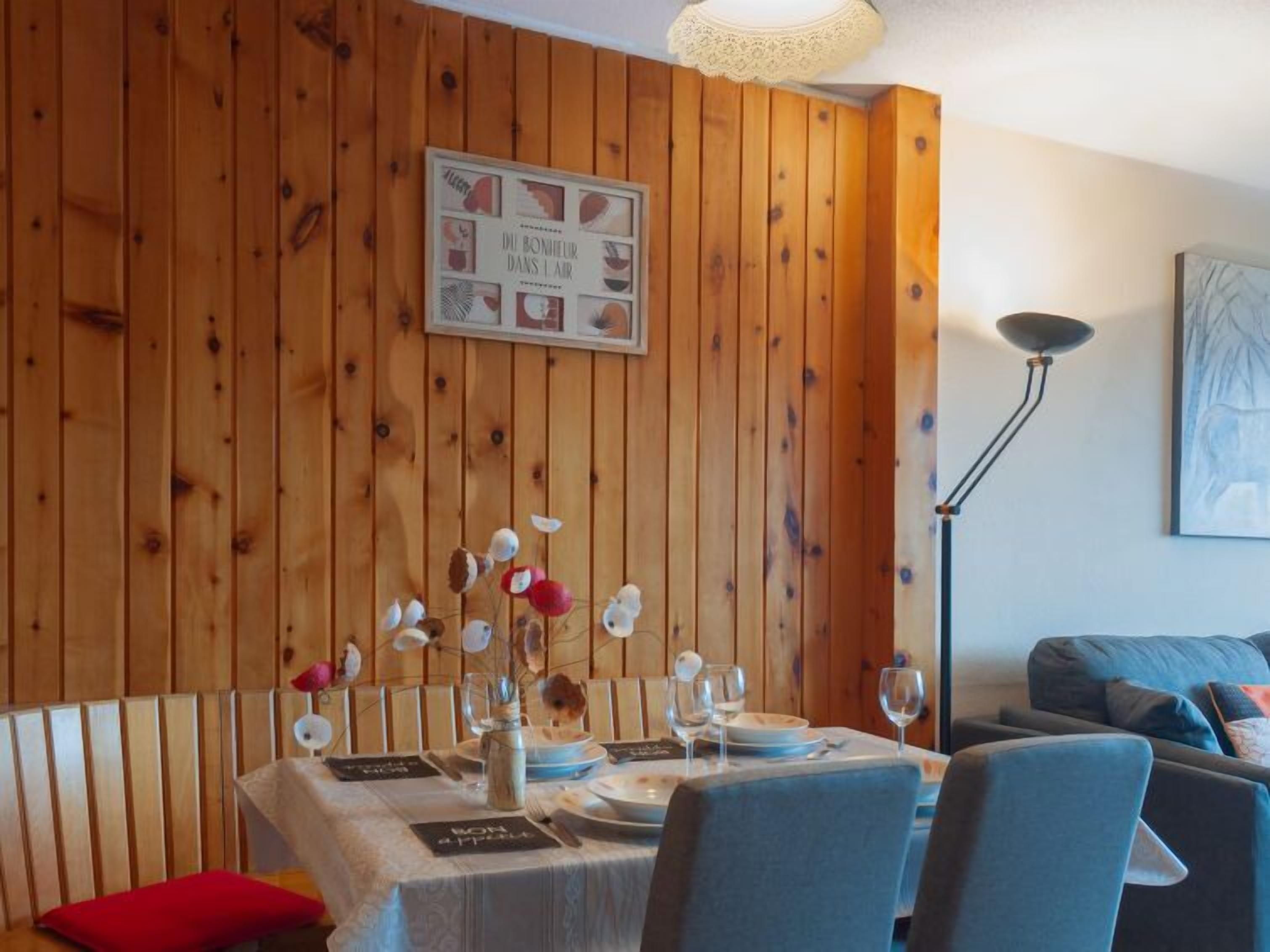 A dining area with a wooden wall, a framed picture, and a table set for four.