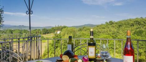 A table with a bottle of wine, a glass, and a plate of salad on a balcony with a scenic view.