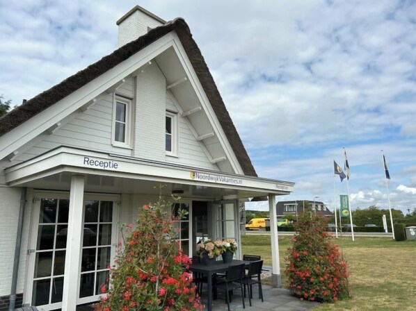A white building with a 'Reception' sign, a covered porch, and two potted plants with red flowers. - Stern Comfort by Interhome (Noordwijk)