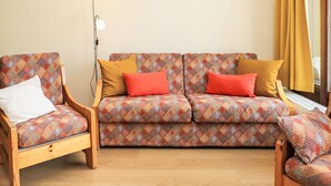 Una sala de estar con un sofá estampado, dos sillones de madera y una lámpara de pie.