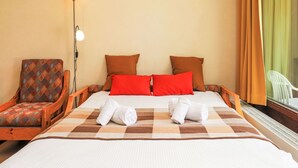 Una habitación de hotel con una cama, dos almohadas, una silla, una lámpara y un ventanal con cortinas.