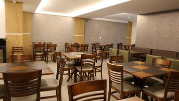A modern dining area with multiple tables and chairs, wooden paneling on the walls, and a neutral color palette.