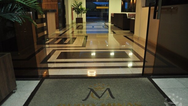 A hotel entrance with a polished floor, a reception desk, and a plant.