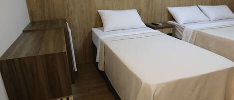 A hotel room with two beds, a wooden headboard, a small bedside table, and a wooden bench.