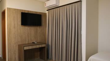Ett hotellrum med ett skrivbord i trä, en platt-TV som är monterad på väggen och ett stort fönster med vertikala persienner.