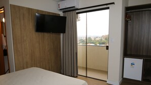 A hotel room with a bed, a television, a sliding door to a balcony, and a small refrigerator.