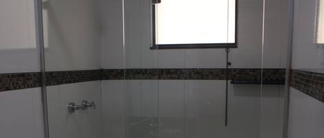Un box de ducha con paredes de vidrio, un inodoro blanco y una pequeña ventana sobre la ducha.