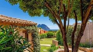 Una villa con techo de tejas, pared de piedra y vistas a la montaña y al mar.