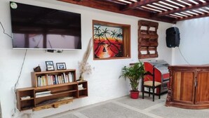 A living room with a flat-screen TV mounted on the wall, a bookshelf, a potted plant, a red chair, and a wooden cabinet.