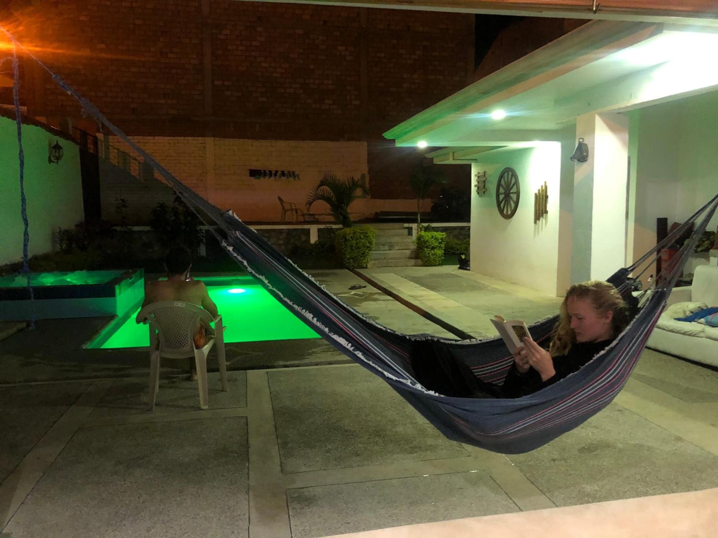 Una persona descansando en una hamaca junto a una piscina, con un niño cerca.