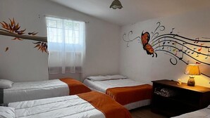 A hotel room with three beds, a window with sheer curtains, a wall mural of a butterfly, and a bedside table with a lamp.