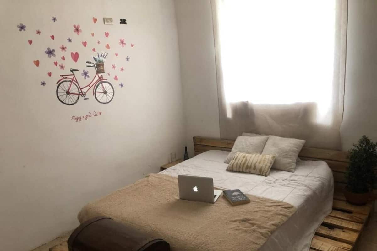 A bedroom with a bed, a laptop, a suitcase, and a wall decal of a bicycle.