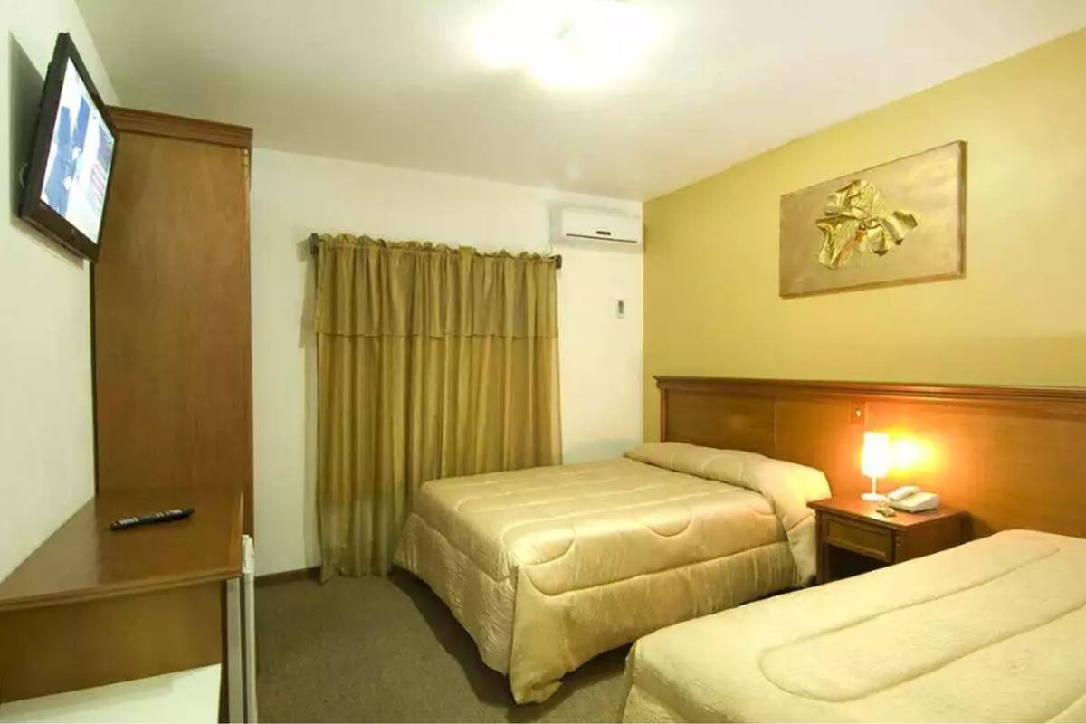 A hotel room with two beds, a wooden wardrobe, a television, a curtain, and a painting on the wall.