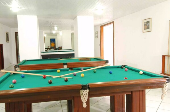 Una mesa de billar con bolas y tacos, un espejo en la pared y una puerta que da a otra habitación.