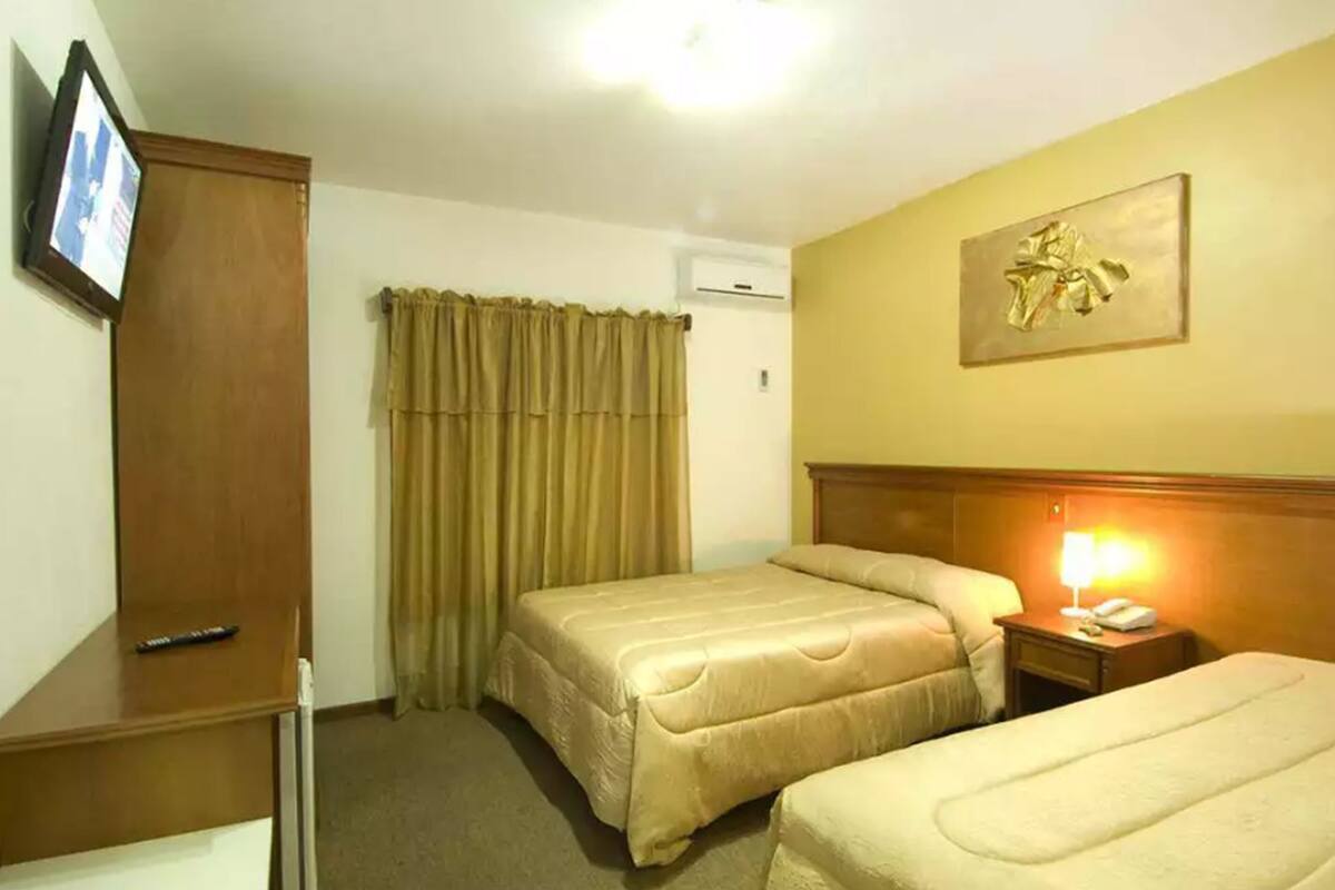 A hotel room with two beds, a TV, a painting, and a lamp.
