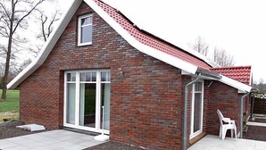 A modern brick house with a sloped roof, large sliding glass doors, and a small patio area with outdoor furniture.
