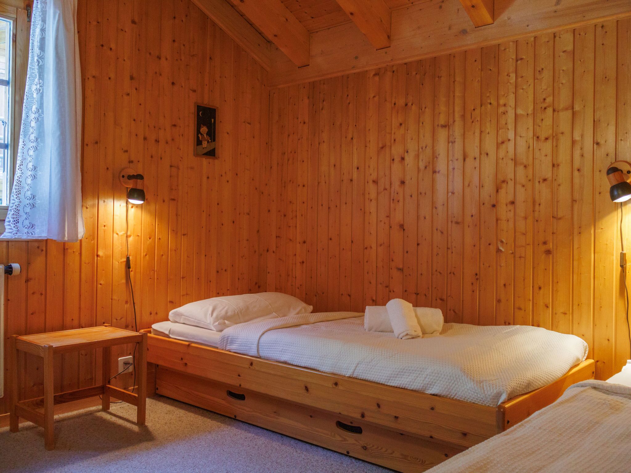 Une pièce en bois avec un lit, une petite table et une lampe fixée au mur.