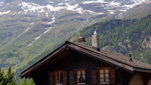 A wooden cabin with a sloped roof, set against a backdrop of snow-capped mountains and a forested valley. - Notre Rêve by Interhome (Zinal)