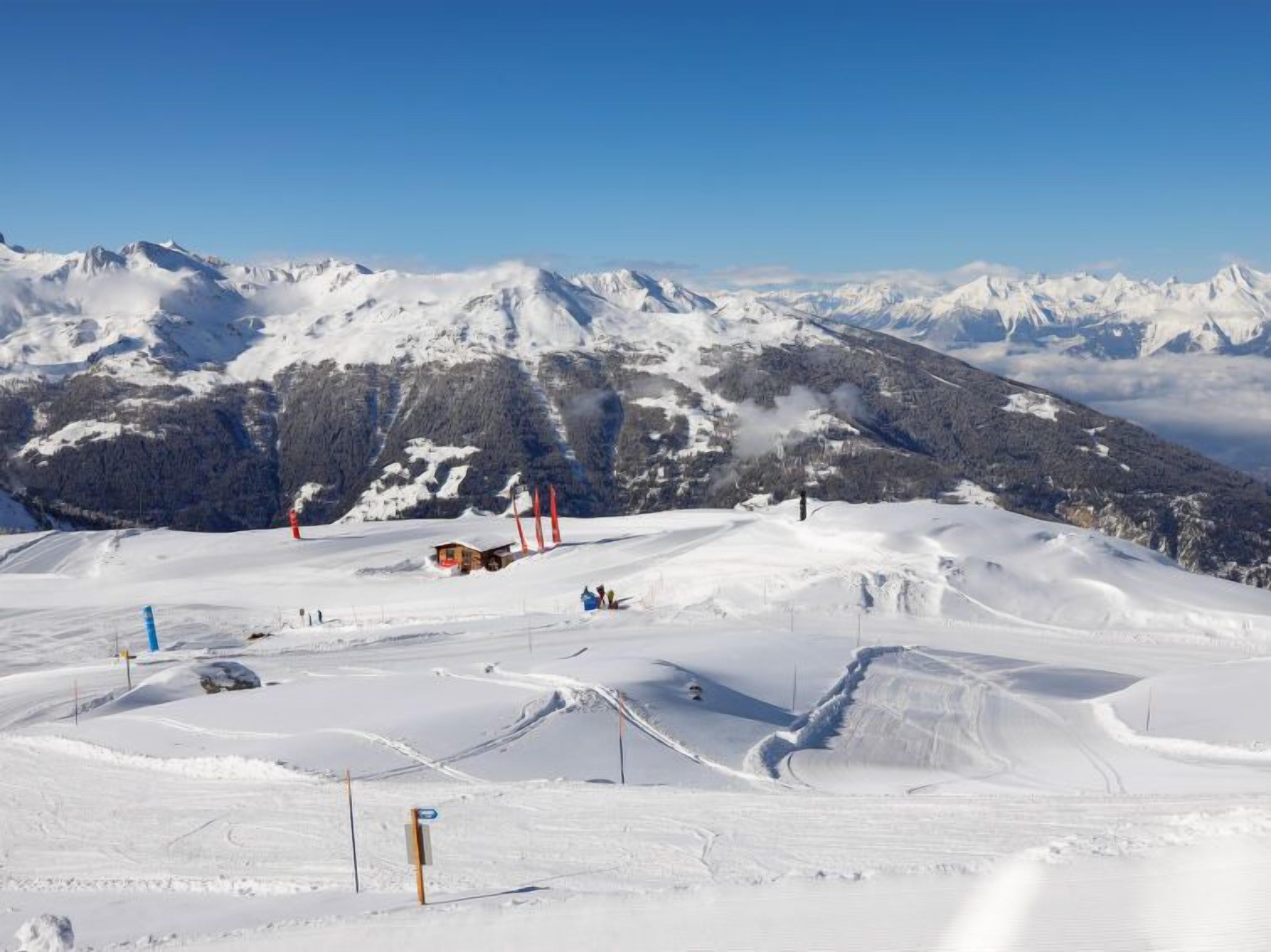 Pista de esqui coberta de neve, com uma pequena estalagem e um teleférico ao fundo.