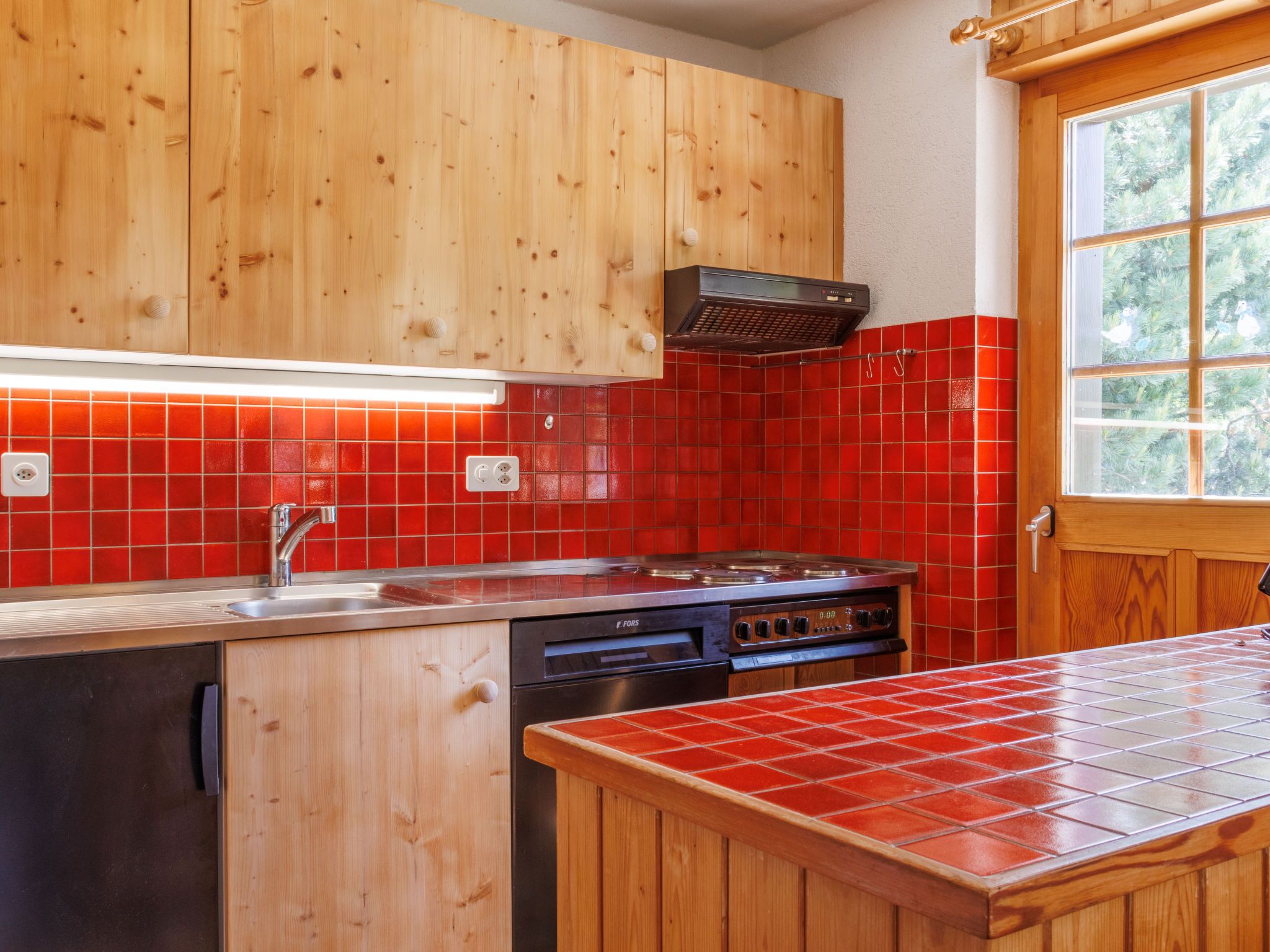 Une cuisine avec des meubles en bois, un crédence en carreaux rouges, une cuisinière en acier inoxydable et un lave-vaisselle.