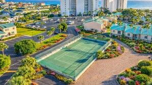 A residential area with a tennis court, palm trees, and buildings with blue roofs. - Spacious, Relaxing, Family-Friendly Townhouse Retreat Steps from Pool & Beach (Destin)