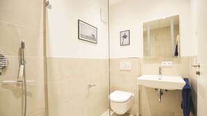 A modern bathroom with a glass shower enclosure, a white toilet, and a sink with a mirror above it. - Modern apartment near downtown (Munich)