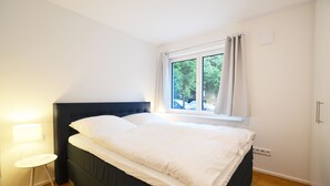 A bedroom with a bed, a window, a lamp, and a small table. - Modern apartment near downtown (Munich)
