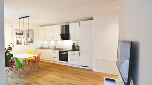 A modern kitchen with white cabinets, a black range hood, and a dining area with a white table and colorful chairs. - Modern apartment near downtown (Munich)