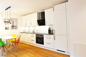 A modern kitchen with white cabinets, a black oven, and a dining area with colorful chairs.