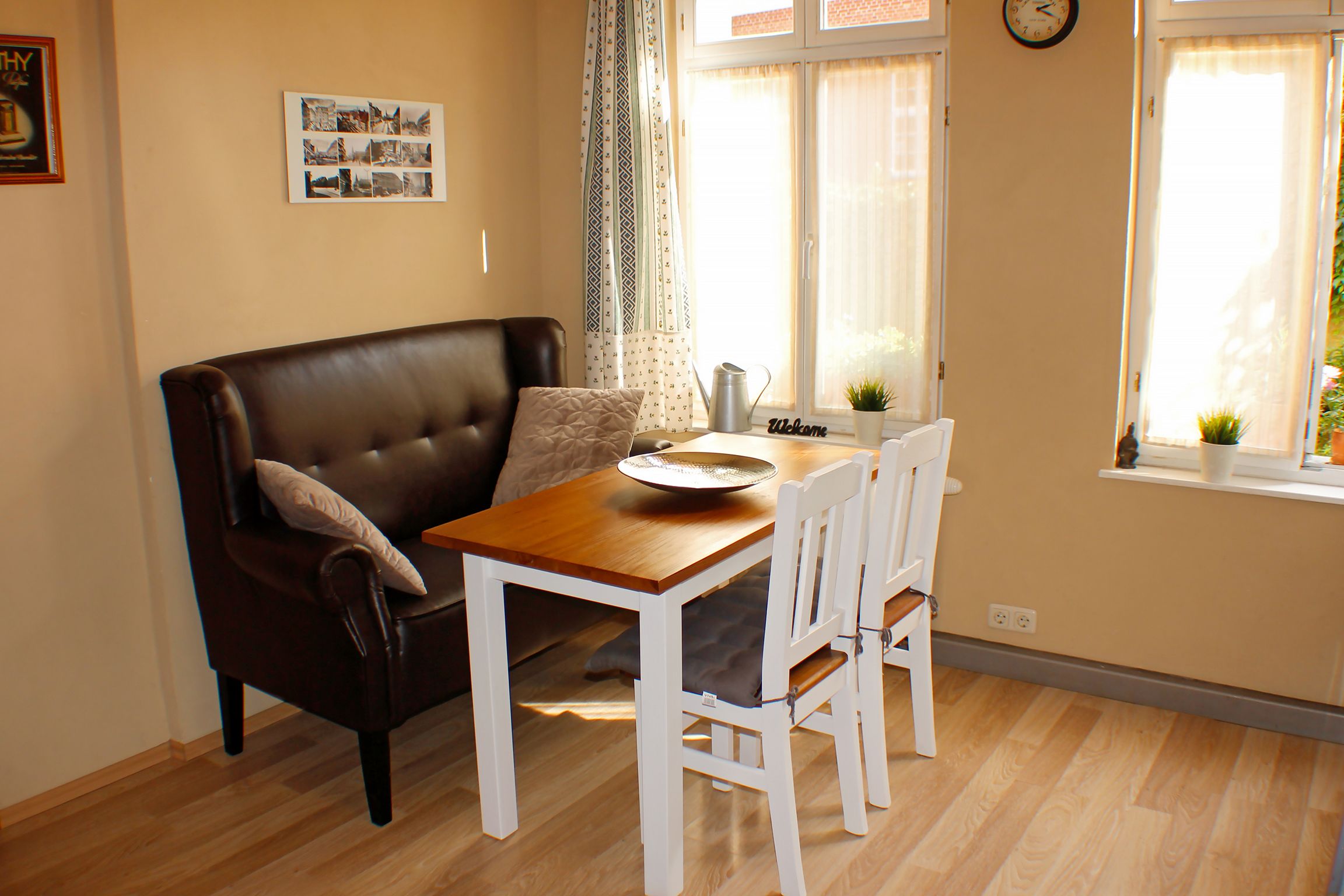 A cozy living room with a brown leather sofa, a wooden dining table, and white chairs.