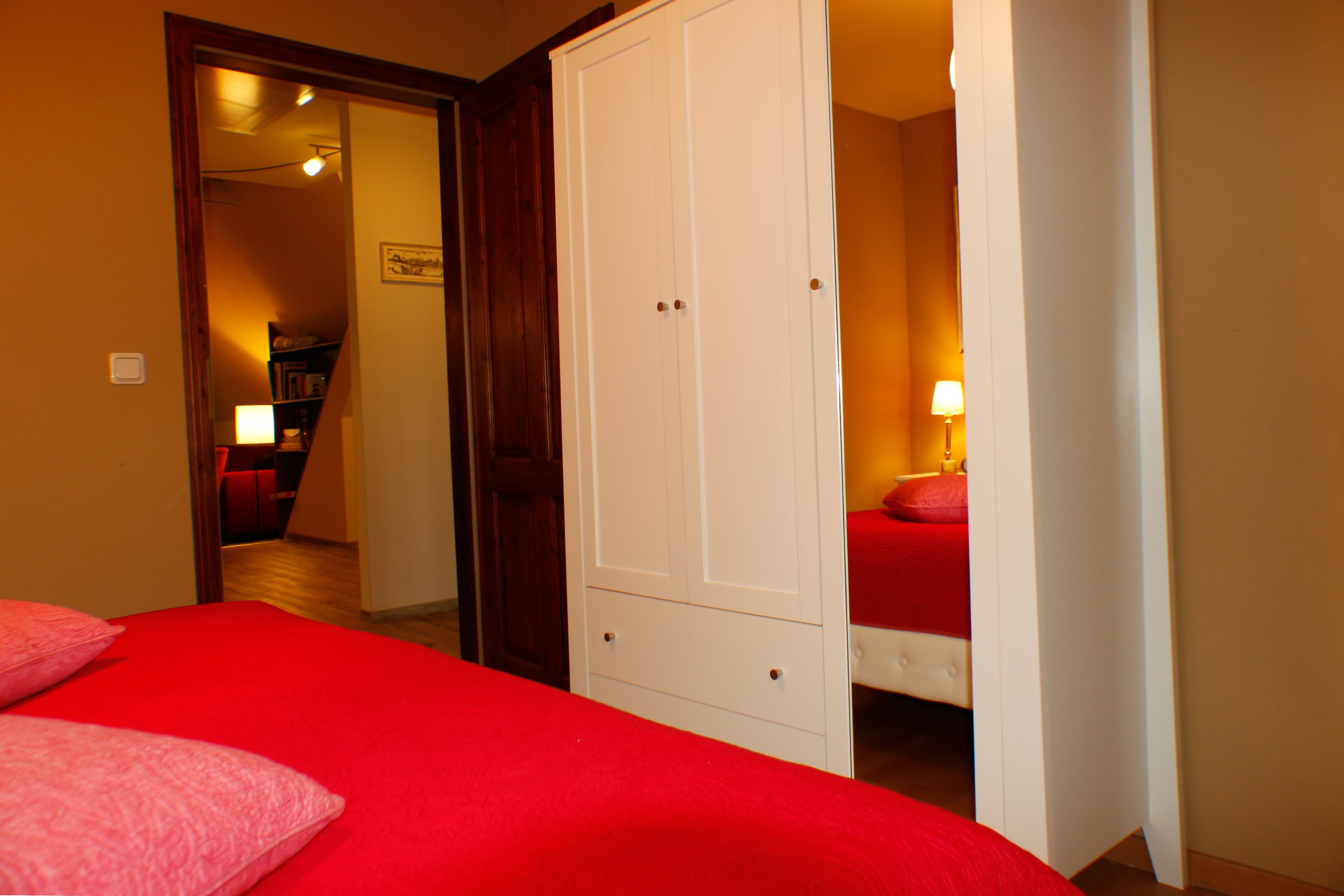 Une chambre avec une couvre-lit rouge, une armoire blanche et une chaise rouge.