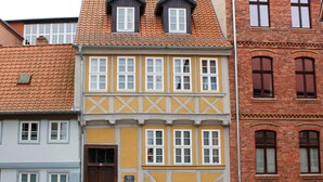 A row of traditional European buildings with distinct architectural styles, including a yellow facade with white window frames and a red-tiled roof. - Ferienwohnungen Stobenstrasse (Quedlinburg)