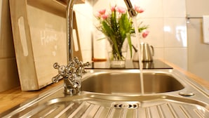 A kitchen sink with a modern faucet, a wooden cutting board, and a vase with flowers on the counter. - Ferienwohnungen Stobenstrasse (Quedlinburg)