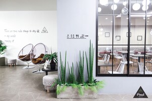 Un interior moderno con una zona de estar que incluye dos sillones huevo, una mesita redonda y una planta en maceta. Se ve una pared con un cartel y un ventanal grande que muestra un comedor.