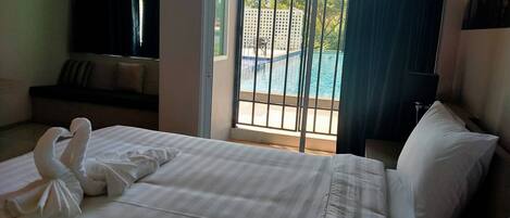 Habitación de hotel con cama, sofá y vista a una piscina a través de una ventana.
