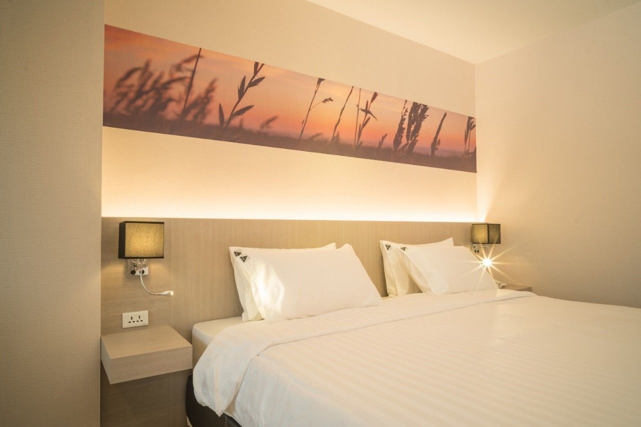 Habitación de hotel con una cama grande, dos lámparas de noche, una mesita de noche y un cuadro colgado en la pared.