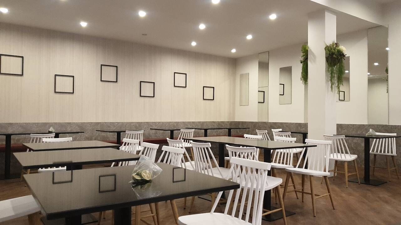 A restaurant with multiple tables and chairs, framed pictures on the wall, and hanging plants.