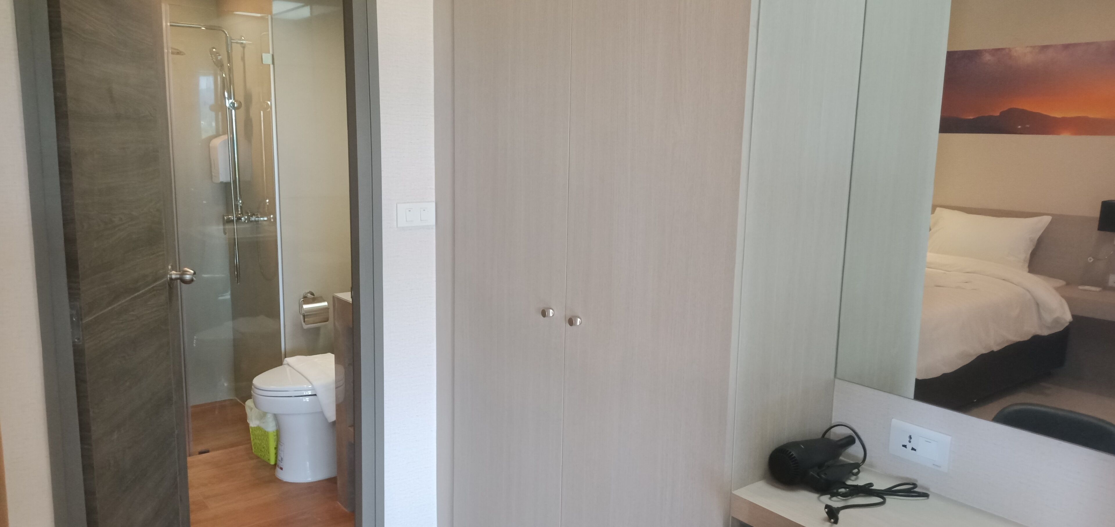 A hotel room with a shower, toilet, and a bed with a headboard.