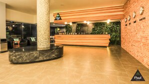 A reception area with a wooden reception desk, a large pillar, and a brick wall with clocks. - Proud Khaoyai (Pak Chong)
